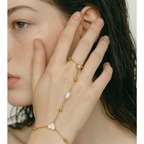 Bracelet de main doré avec perle naturelle et cœur pavé de zircons, porté sur une main féminine